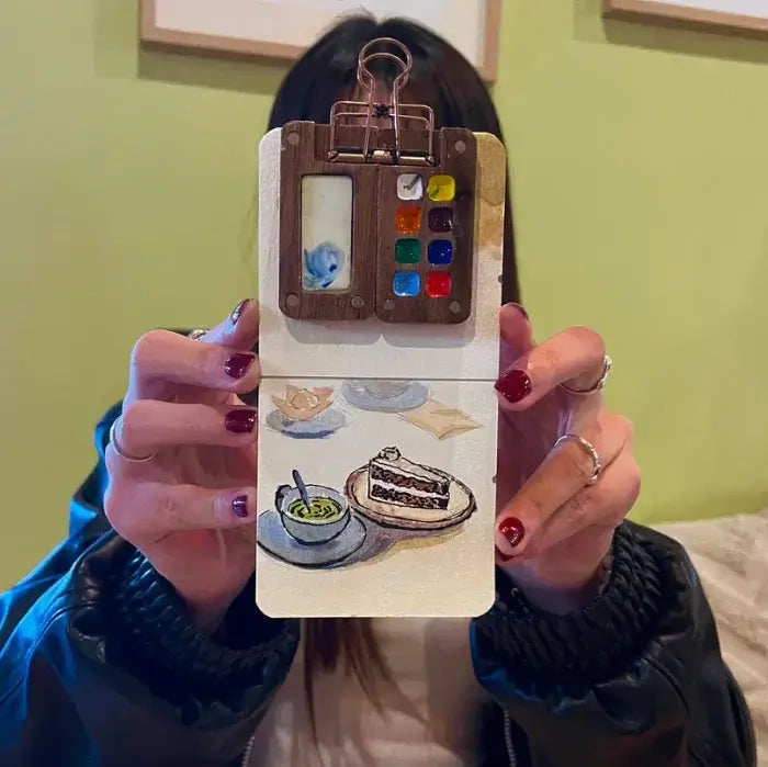 On-the-go watercolor tools with secure clip holder, great for plein air art, held in a traveler's hand.