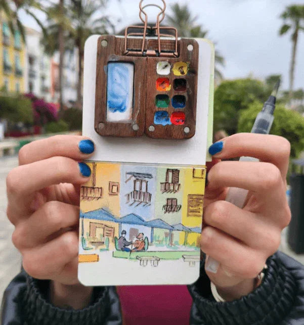 Pocket-sized painting set with mixing space, used in nature journaling, displayed on a sketchbook.